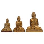 Three Oriental gilt decorated wooden figures, depicting a seated Buddha, ornated with semi-precious