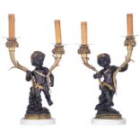 A pair of patinated and gilt bronze candlesticks shaped as putti holding horns of plenty, on Carrara