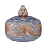 A Japanese inspired ceramic covered bowl, decorated with koi and on top a sitting figure, signed and