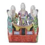 A Chinese famille rose porcelain group depicting five standing sages reading a scroll in a fenced ga