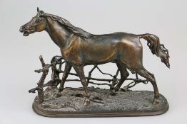 Pferdeskulpur, stehender Hengst am Gatter, auf naturalistisch gestalteter Plinthe, wohl Bronze um