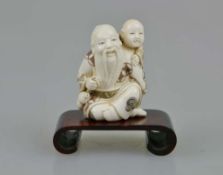 Netsuke, Japan, wohl 19. Jh., sitzender, alter Mann mit Kind auf der Schulter, Elfenbein, am Boden