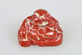 Okimono, Japan, wohl 19. Jh., sitzender Buddha Hotei, roter Stein, H.: ca. 3,5 cm.