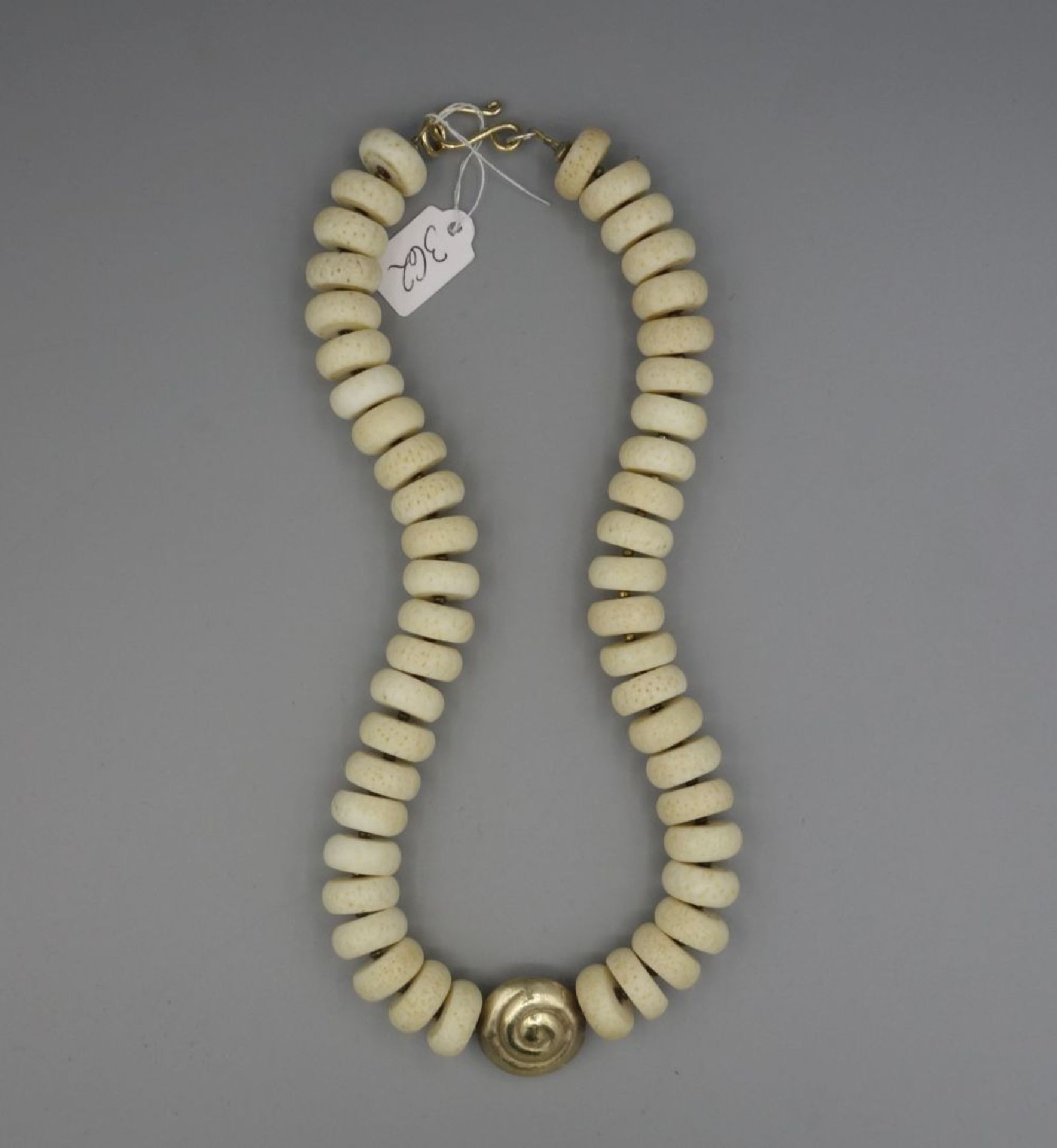 KETTE / BEINKETTE / necklace, mit gold- und silberfarbenen Metallanteilen. Im Zentrum spiral- oder