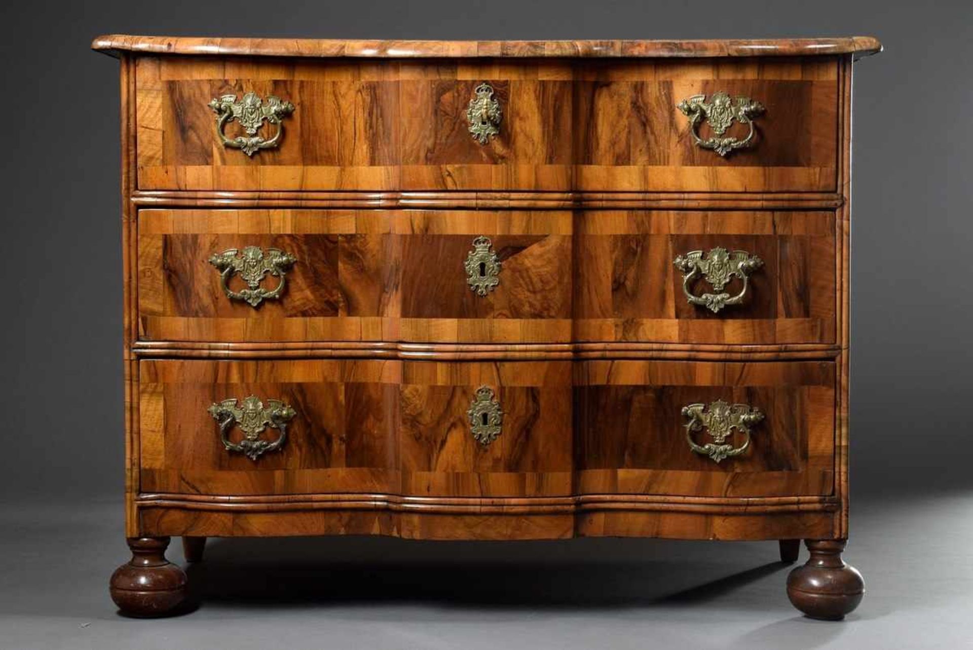 Strict baroque commode with gilded fittings, curved front and 3 drawers, on pressed ball feet and
