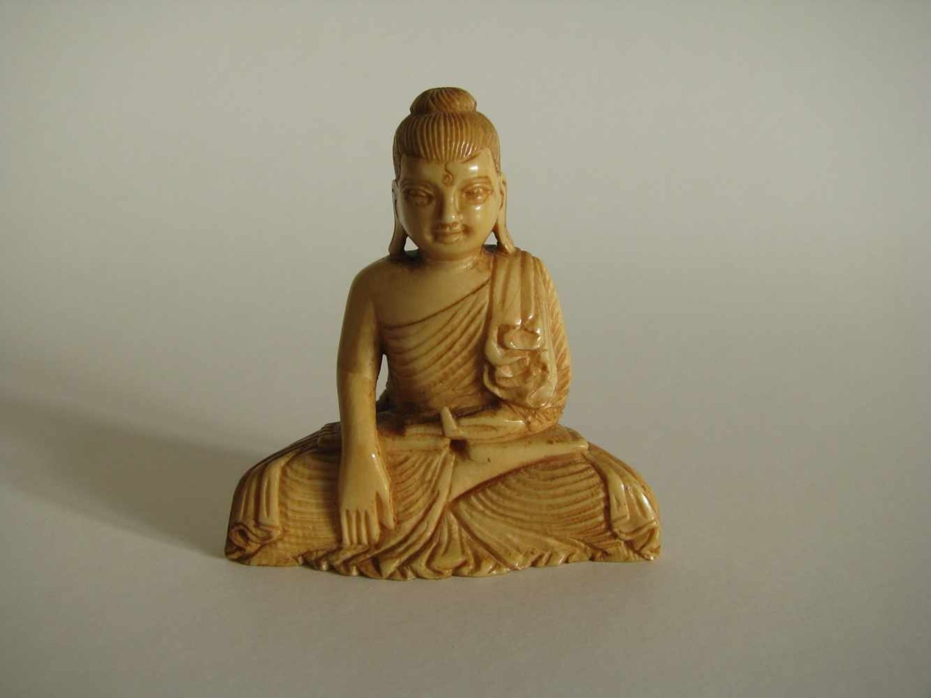 Sitzender Buddha, wohl Ceylon, 19. Jahrhundert, Elfenbein beschnitzt, 5,5 x 5,5 x 2,4 cm.