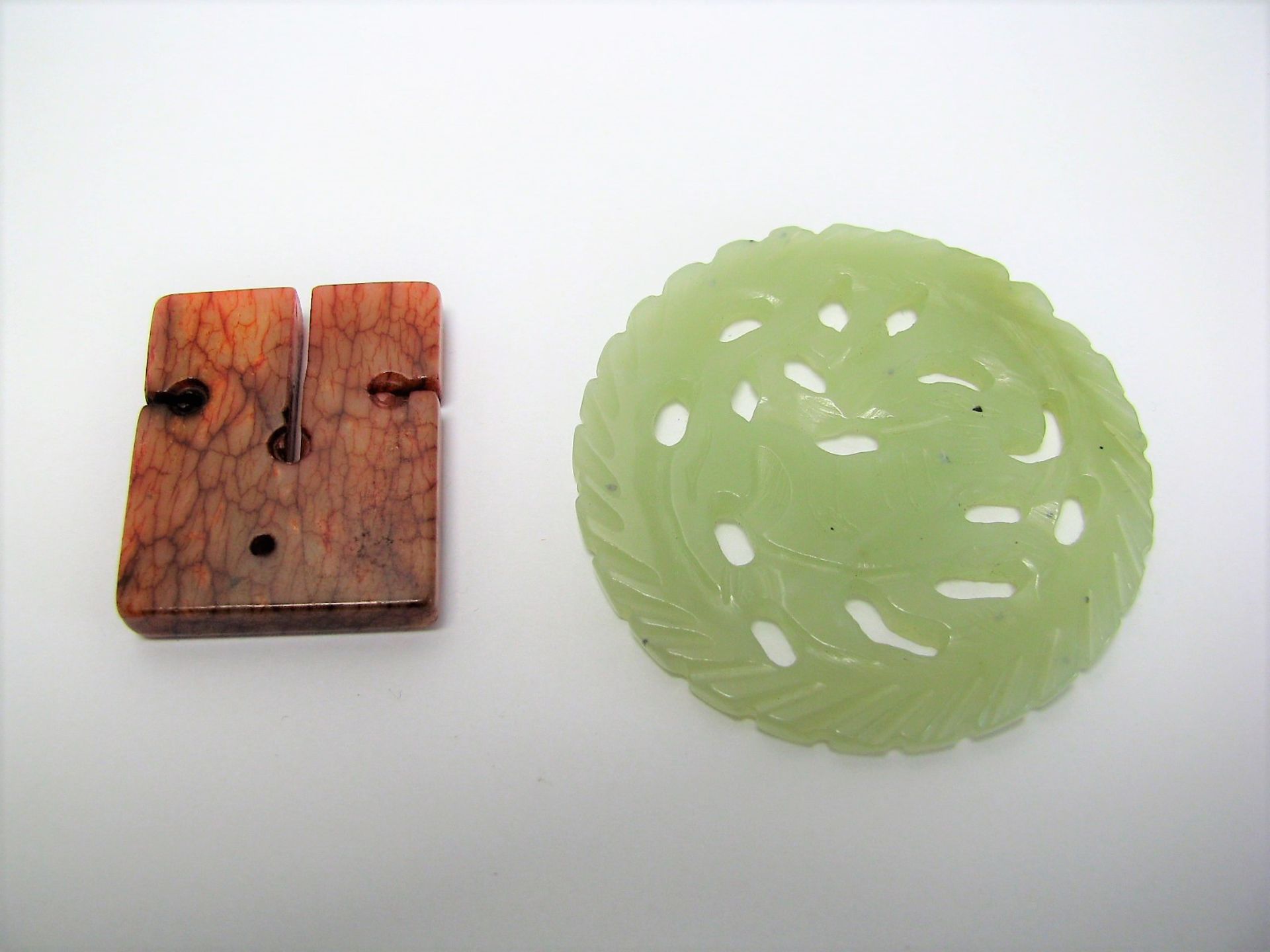 2 Jadestücke, China, grünliche und rötliche Jade, 1 x d 5,5 cm, 3,5 x 3 cm.