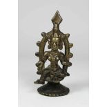 Kleine Bronzefigur, eine Gottheit mit drei Brüsten, auf Sockel sitzend, ein Bein angewinkelt, im