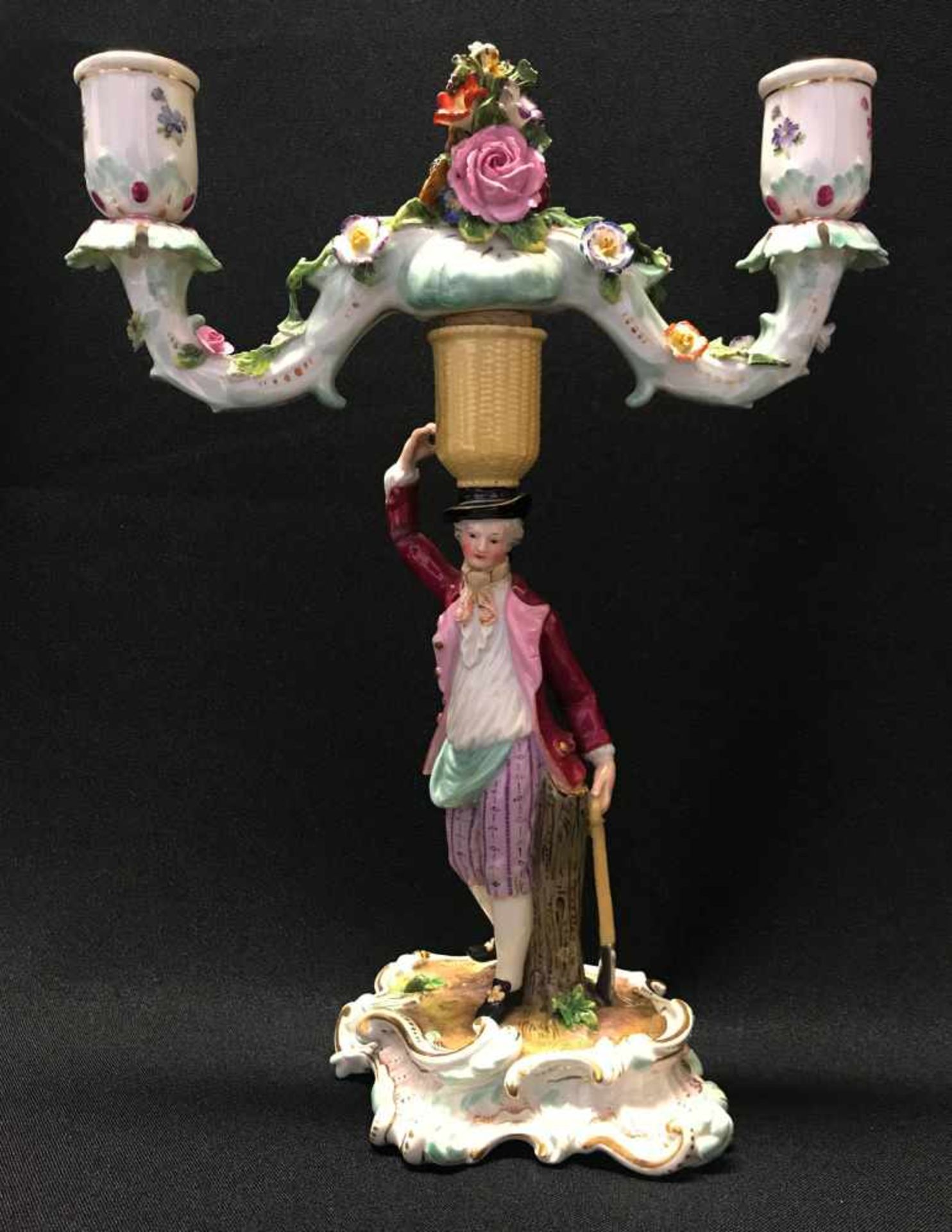 Meissen, Kerzenständer, zweiarmig mit Mann, Porzellan, farbig staffiert. In der linken Hand hält
