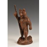 A Black Forest carving, of a bear, he stands upright, holding a staff, 23cm high,
