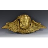 A Continental giltwood architectural cresting, carved as a winged putto mask, 69cm wide,