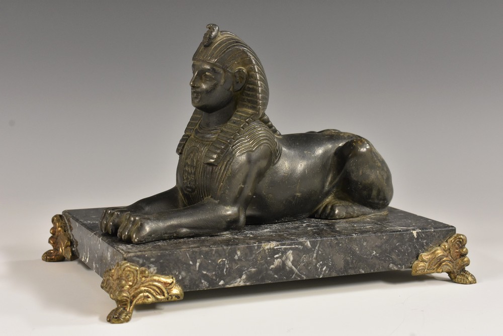 A French dark patinated metal desk model, of a sphinx, gilt metal mounted rectangular marble base,