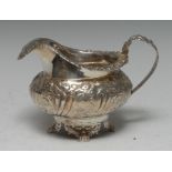 A George IV silver cream jug, embossed with foliate scrolls, resting on four claw feet, 10cm high,