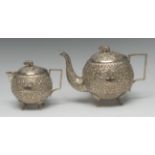 An Indian white metal globular teapot and water jug, profusely chased with dense scrolling foliage,