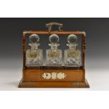 A Victorian oak three bottle Tantalus, hobnail cut, prismatic stoppers, plated mounts, c.