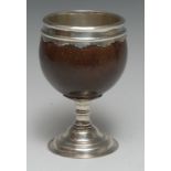 A George III silver coloured metal lined and mounted pedestal coconut cup, shaped pendant border,