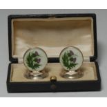 A pair of George V silver and enamel menu holders, decorated in polychrome with Scottish thistles,