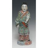 A Chinese porcelain figure, of a musician, he stands in flowing robes holding a bamboo flute,
