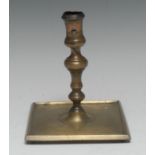 A 17th century French brass candlestick, waisted sconce, knopped stem, broad square base,