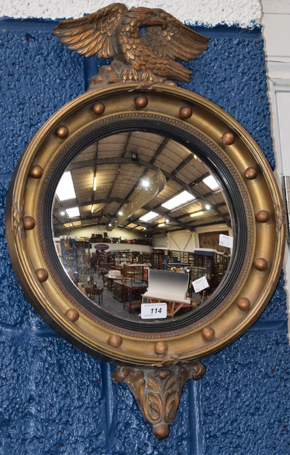 A gilt framed circular convex mirror, the mount applied with spheres, surmounted by an eagle,