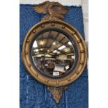 A gilt framed circular convex mirror, the mount applied with spheres, surmounted by an eagle,