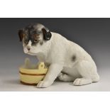 A Gebruder Heubach bisque model, of a young dog, seated by a coopered pail, 14cm high,