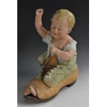 A Gebruder Heubach bisque piano baby, of a young boy seated in an old boot, 30cm high,