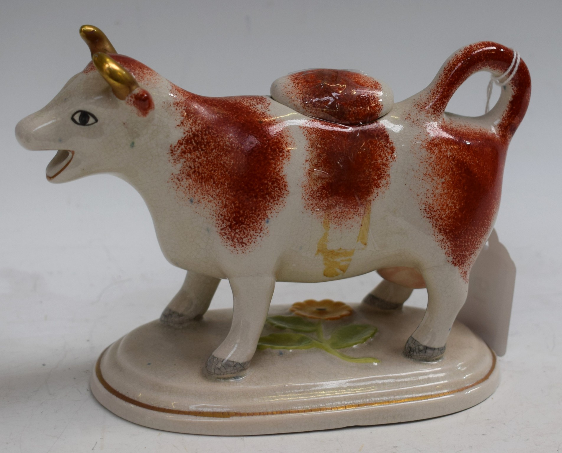 An early 20th century cow creamer and cover, with rust markings, oval base,