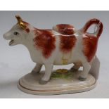 An early 20th century cow creamer and cover, with rust markings, oval base,