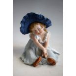 A Gebruder Heubach bisque piano baby, of a seated young girl, wearing a large blue bonnet,