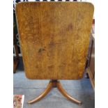 A George III oak tilt top table, rounded rectangular top, turned column, three sabre legs, bun feet.