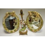 A pair of continental porcelain oval wall mirrors, applied in relief with cherubs and flowers,