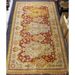 A hand woven Middle Eastern throw rug decorated in tones of red and burnt Sienna on a beige ground.