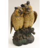 A large Austrian cold painted terracotta model, of a pair of owls seated on a branch, glass eyes,