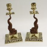 A pair of brown patinated and polished brass candlesticks, each stem cast as a dolphin,