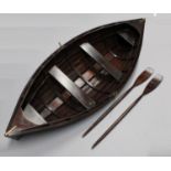A large scratch built model of a rowing boat, brass bound and stained as mahogany, oars ensuite,