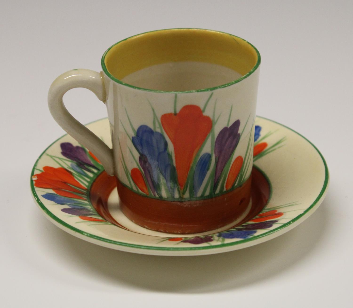 A Clarice Cliff Crocus coffee cup and saucer, decorated with orange, blue and purple flowers,