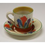 A Clarice Cliff Crocus coffee cup and saucer, decorated with orange, blue and purple flowers,