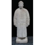 A Chinese marble figure, carved as a man in a traditional tunic and fur hat, rectangular base, 57.