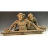 A pair of plaster door figural crestings, of Medieval jesters, in buff and washed black,