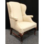 A George I style wingback armchair, stufffed over upholstery, H-stretcher, cabriole forelegs,