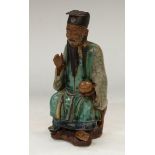 A Chinese stoneware figure, of an immortal, seated, holding a peach, glazed in mottled tones of