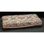 A large rounded rectangular foot stool, upholstered in a floral multi-colored Roses lattice pattern,