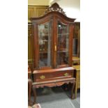 A reproduction teak display cabinet, pierced and shaped pediment to arched top, two glass doors