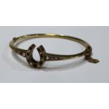 A gold hinged bangle, the centre as a horse shoe set with seed pearls and ruby chips, unmarked, 8.4g