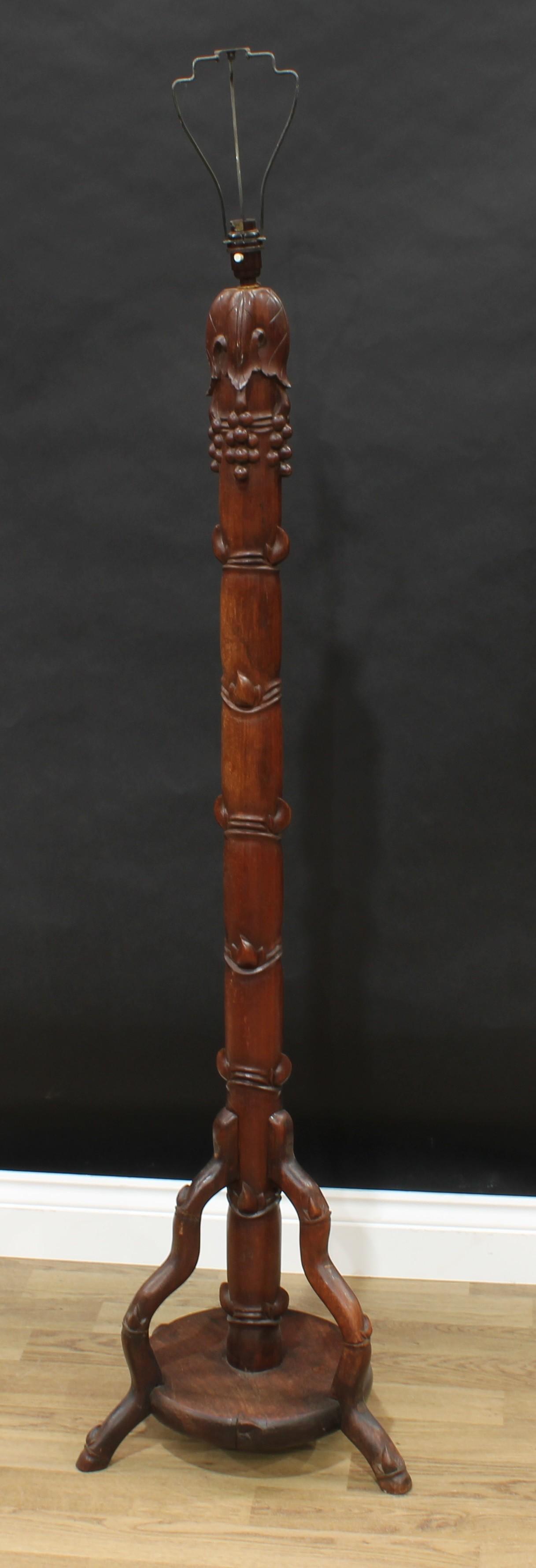 A Chinese hardwood standard lamp, carved with leafy bamboo and fruiting vine, circular tripod
