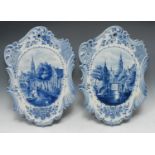 A pair of Dutch cartouche shaped wall plaques, decorated in blue with town scenes, 51cm x 35cm