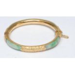 A jade inset yellow metal hinge bangle, four panels of stained jade green stone, inset to a