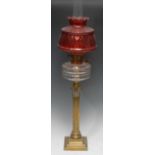 An early 20th century oil lamp, brass Corinthian column, clear glass reservoir, cranberry glass