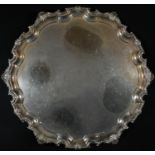 A George III style silver shaped circular salver, piecrust, shell and leafy scroll border, plain